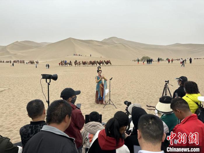 圖為2023年4月底，敦煌大漠“逐舞者”奧楠在鳴沙山月牙泉景區(qū)視頻直播，吸引游人圍觀。　馮志軍 攝